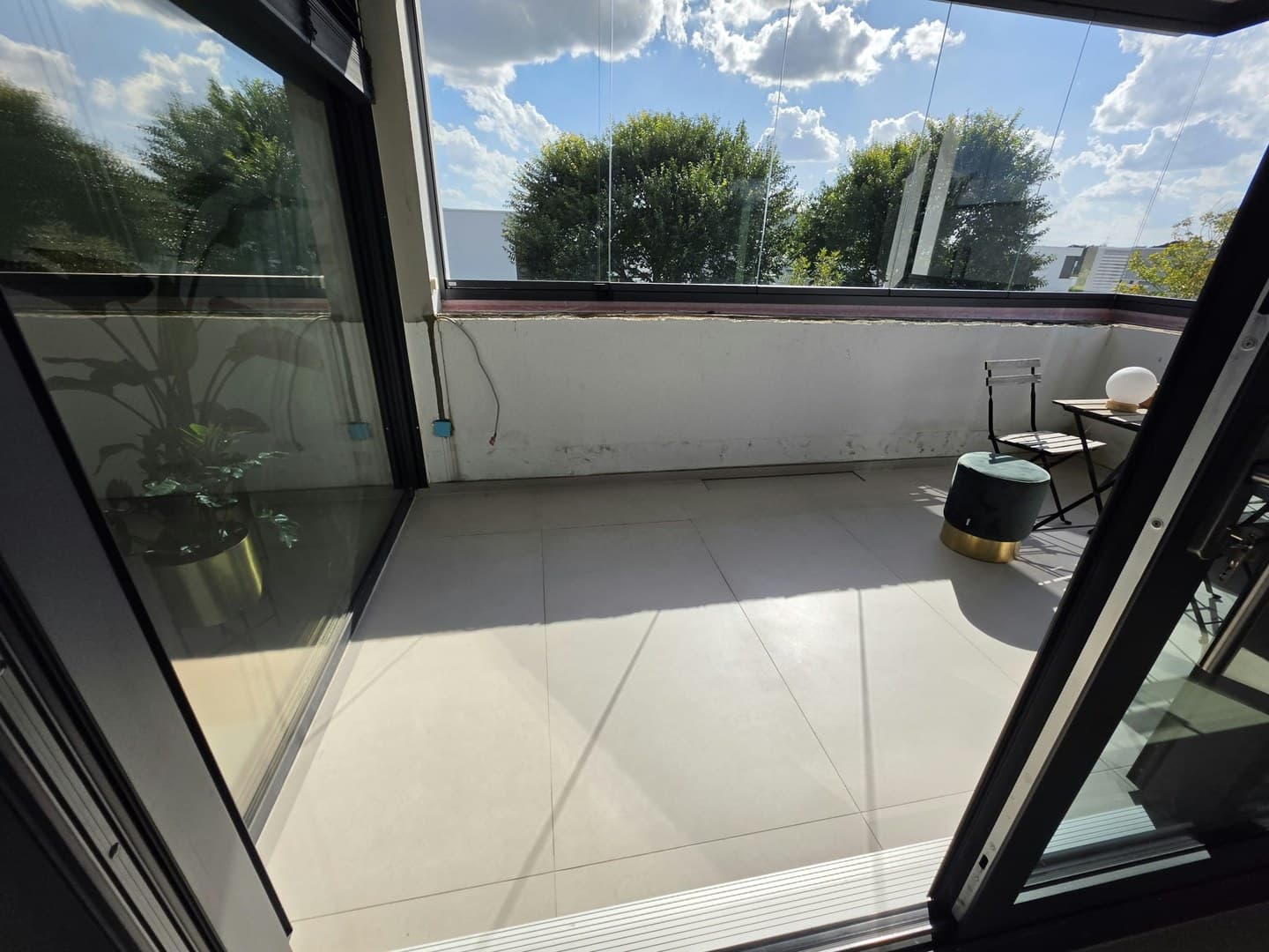 Blick aus dem Wohnraum durch die offene Glastür auf den verglasten Balkon mit hellen Großformat-Fliesen