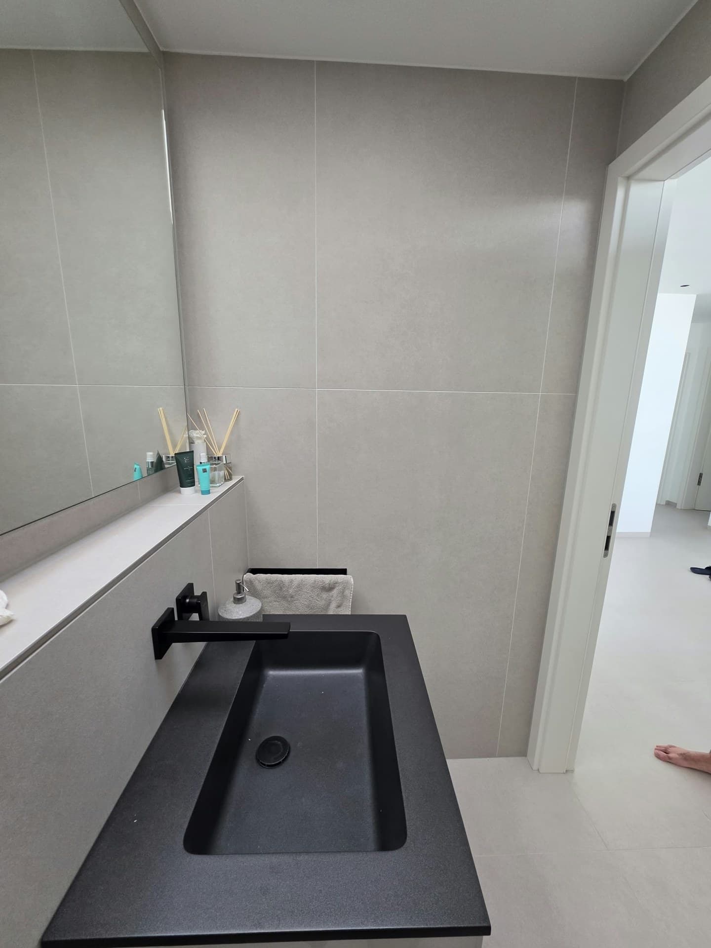 Bad mit großen grauen Wandfliesen und schwarzem Waschbecken
